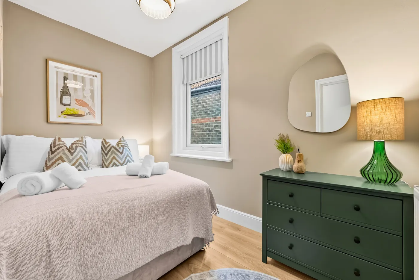 The finished bedroom with warm beige walls, a made bed, a green chest of drawers and a lamp
