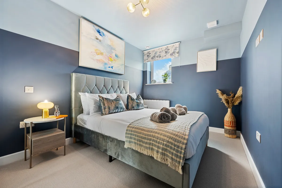 A finished bedroom with navy walls and a grey upholstered bed