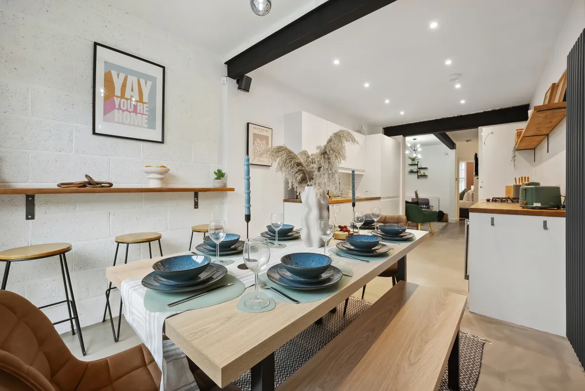 A long oak dining table set with blue tableware under a black beam