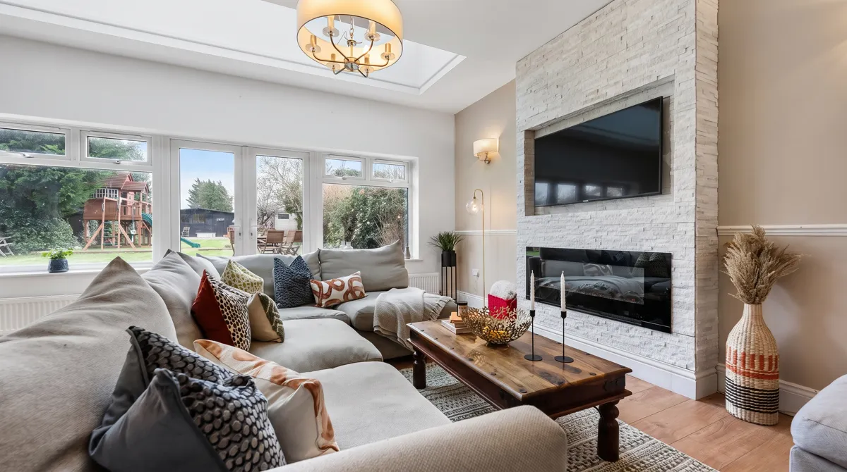 A cream corner sofa facing a white stone fireplace wall, with garden doors behind